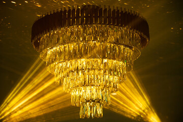 Opulent crystal chandelier illuminates luxurious interior with warm golden glow, casting intricate...