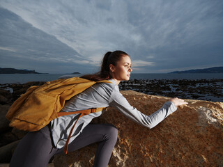 A young woman of Caucasian descent climbing a rocky surface by the sea, showcasing determination...