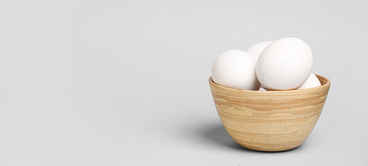 Bowl with raw chicken eggs on grey background