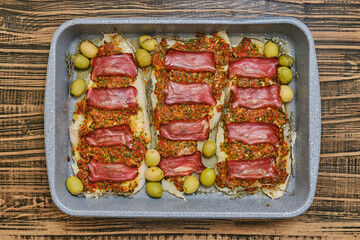 Roasted fish fillets are layered with bacon and herb sauce, accompanied by green olives
