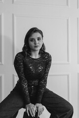 A stylish young woman in a red lace top and high-waisted wide-leg jeans poses confidently against a white paneled wall