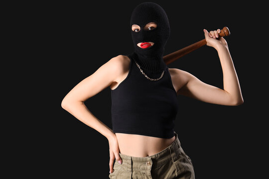 Beautiful young stylish woman in balaclava with baseball bat on black background