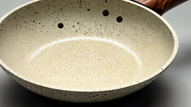 Stylish speckled frying pan with wooden handle on a neutral background