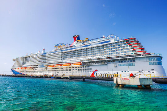 Carnival cruise ship docked in turquoise water Caribbean sea under clear blue sky with lifeboats along white hull near pier. Willemstad. Curacao.