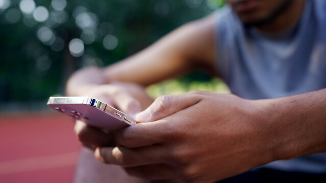 Close-up of an African American athlete sitting on a basketball court, scrolling through his smartphone