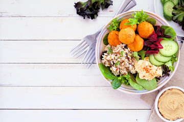 Healthy homemade salad bowl with falafels, hummus, quinoa and vegetables. Top down view table scene on a white wood background with copy space.