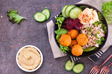Healthy homemade salad bowl with falafels, hummus, quinoa and vegetables. Above view table scene on a dark stone background.