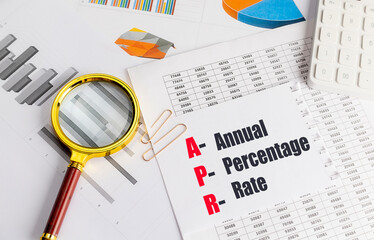 APR acronym for annual percentage rate on a paper with financial charts, magnifying glass, and...