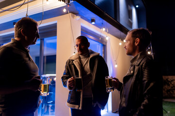 Three Friends Socializing Outside at Night Holding Beer Glasses Under Outdoor Lights