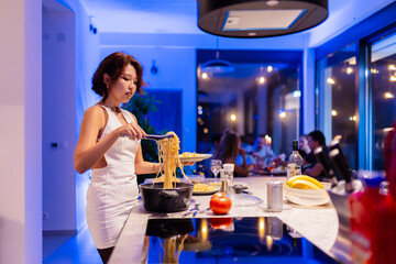 Woman Serving Spaghetti in a Modern Kitchen During a Social Dinner Gathering