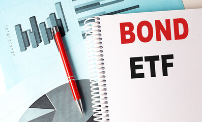 Bond ETF text on a spiral notebook with financial charts and a red pen on a blue background