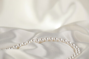 Beautiful pearl necklace on white silk, closeup
