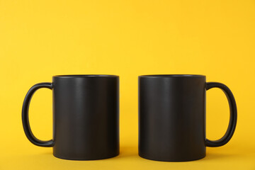 Two blank black mugs on yellow background. Mockup for design