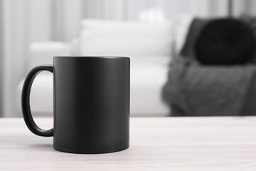One blank black ceramic mug on white wooden table. Mockup for design