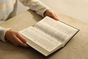Naklejka premium Woman reading Holy Bible at beige table, closeup