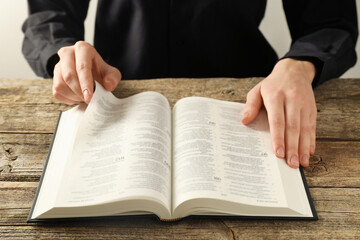 Woman reading Holy Bible in English language at wooden table, closeup