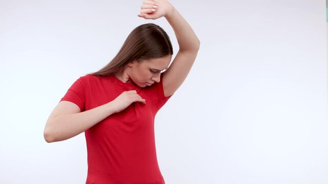 Young beautiful girl in a red T-shirt shows wet armpits. Treatment of hyperhidrosis.