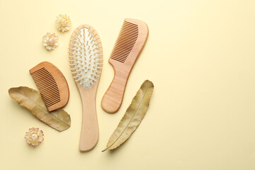 Wooden hair brush, combs, flowers and leaves on beige background, flat lay. Space for text