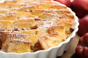Delicious bread pudding with raisins, powdered sugar and apples on wooden table, closeup