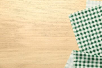 Green checkered tablecloth on wooden background, top view. Space for text