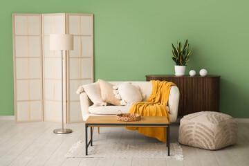 Sofa with pillows, pouf, coffee table and folding screen in living room