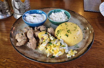 Traditional Moldovan food, meal closeup with pork stew, mamaliga polenta, fried eggs, cheese and sour cream sprinkled with parsley.