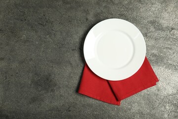 Red napkin and empty plate on grey table, top view. Space for text