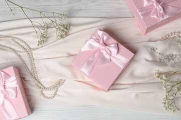 Beautiful wedding gifts, pearl jewelry, dress and gypsophila flowers on light wooden table, flat lay