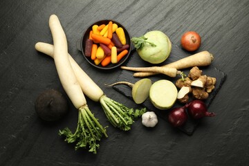 Different raw root vegetables on black table, flat lay
