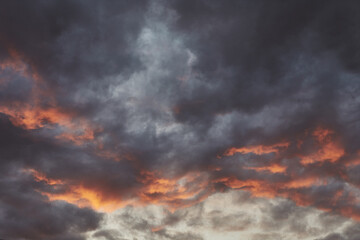 Dark clouds illuminated by sunset hues over a tranquil landscape during twilight hours