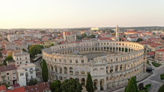 Flight over the Croatian city of Pula at sunrise. Aerial view of the historic Roman amphitheater of Pula, Istria peninsula. Ruins of the Roman Colosseum Arena in Pula, Croatia. UNESCO World Heritage.