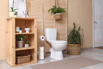 Stylish interior of modern restroom with toilet bowl, shelving unit and plants