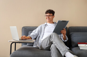 Male accountant working with clipboard and laptop on sofa in office