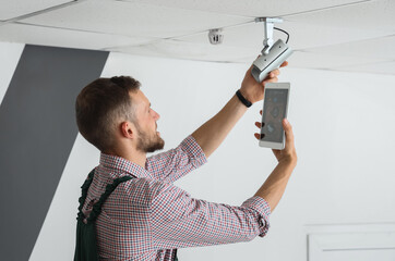 Male worker with tablet computer installing alarm system in room
