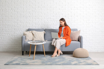Obraz premium Young pretty woman chatting with laptop on grey sofa at home