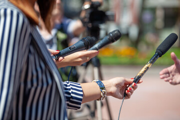 Journalists and TV reporters holding microphones during a press conference or media event with a...
