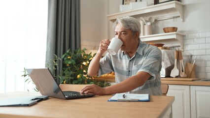 Smart senior business man looking at laptop while drinking hot coffee. Elder project manager making...