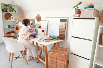 Female fashion designer taking thread spool at table in studio