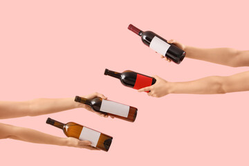 Female hands holding bottles of wine on pink background