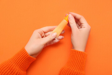 Female hands with cosmetic product on orange background, closeup