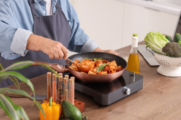 Senior woman frying pasta with meat in kitchen, closeup