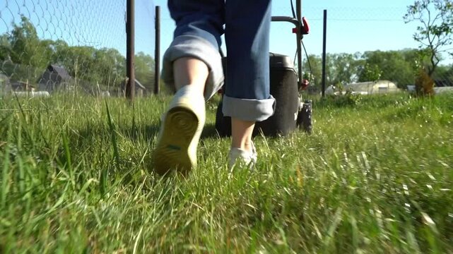 Woman with a lawnmower mows the lawn at the dacha