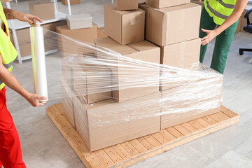 Male loaders wrapping boxes on pallet with stretch film in warehouse