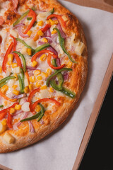 Close-up view of a pizza with vegetables on a cardboard box ready for delivery.