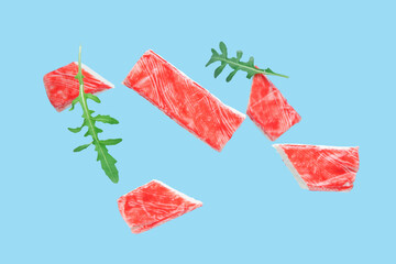 Tasty crab sticks and arugula leaves flying on blue background