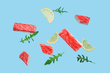 Tasty crab sticks with arugula leaves and slices of lemon flying on blue background © Pixel-Shot