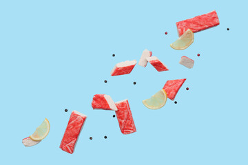 Cut tasty crab sticks with peppercorns and slices of lemon flying on blue background © Pixel-Shot