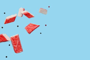 Cut tasty crab stick and peppercorns flying on blue background © Pixel-Shot