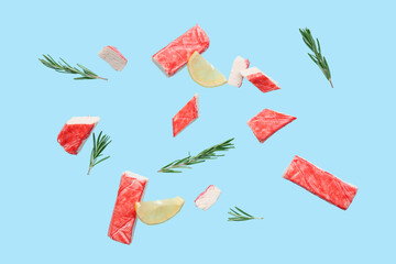Cut tasty crab sticks with rosemary and slices of lemon flying on blue background © Pixel-Shot