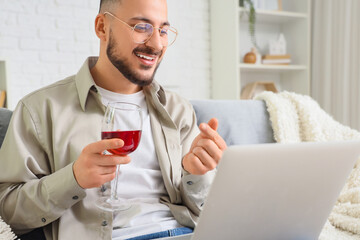 Young man drinking wine and video chatting with girlfriend at home. Online dating